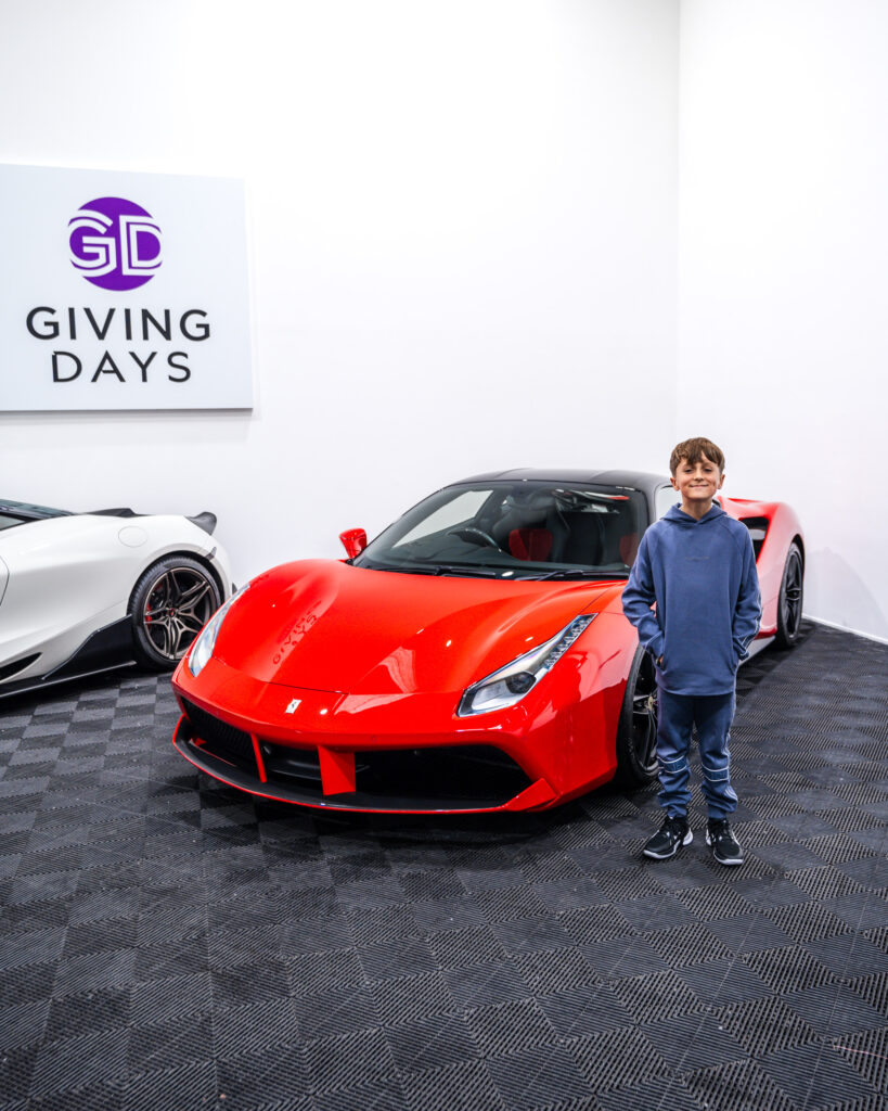 A child standing in front of a red ferrari car
